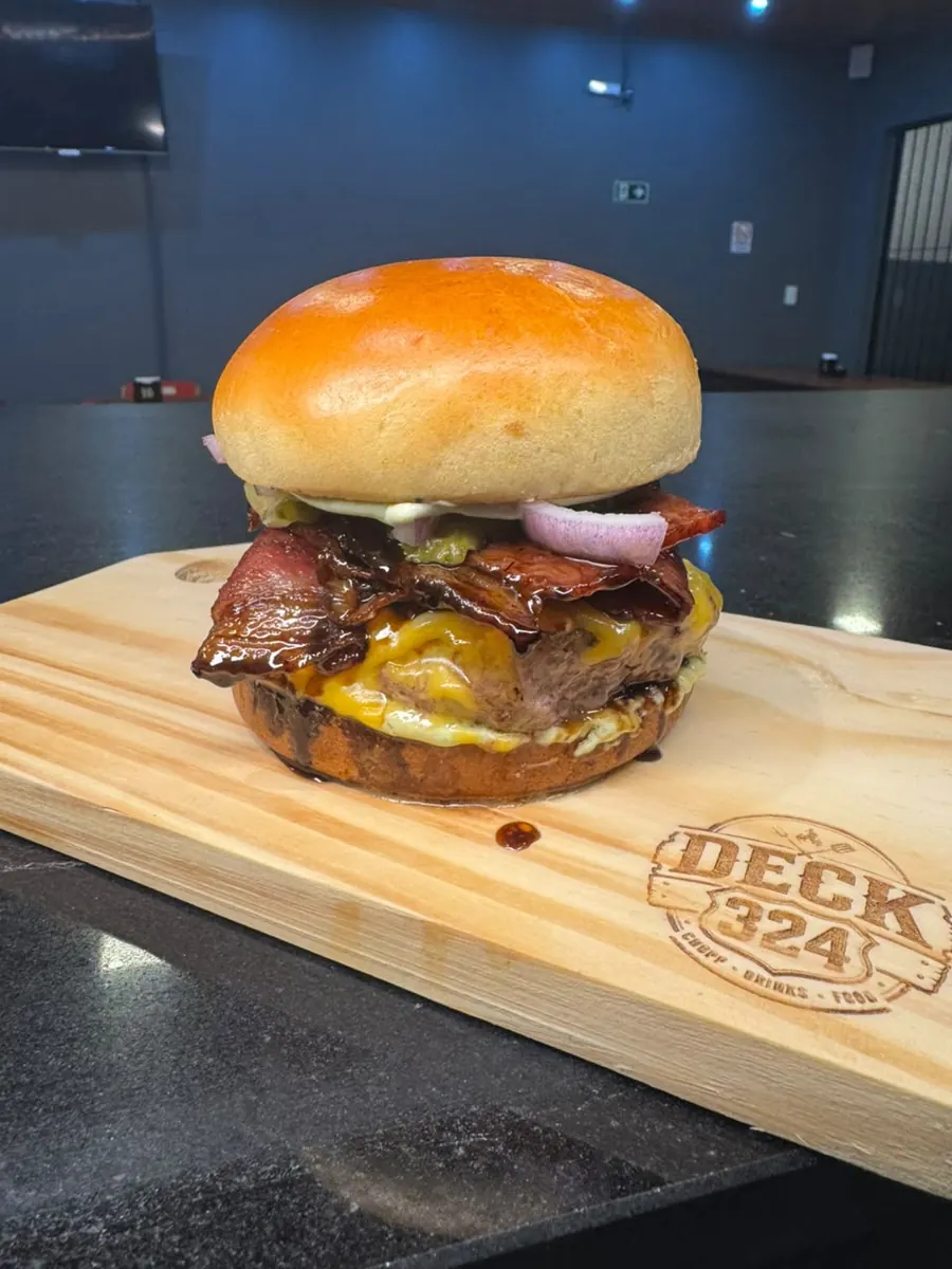 Hambúrguer com cheddar, bacon e cebola roxa no pão brioche, sobre tábua com a marca Deck 324